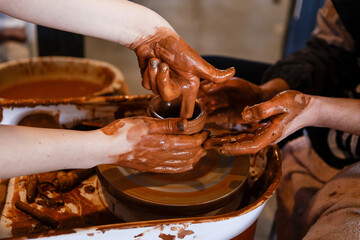 potter with a student on the potter's wheel makes dishes from clay