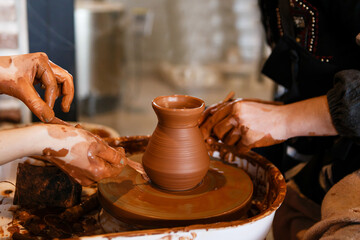 Fototapeta na wymiar potter with a student on the potter's wheel makes dishes from clay