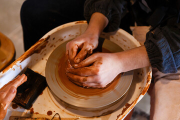potter with a student on the potter's wheel makes dishes from clay