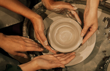 three women are working on a potter's wheel, making a vase.
