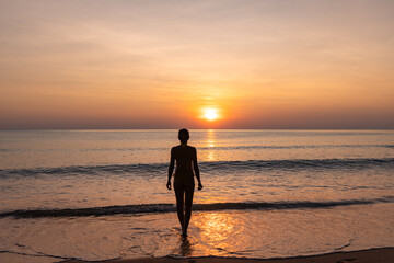 Fototapeta na wymiar Silhouette of woman in an orange sunset on the beach