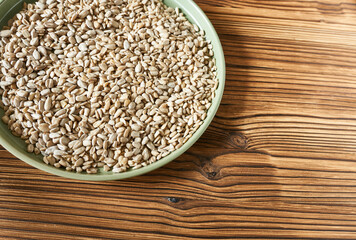Peeled sunflower seeds in a green plate on a wooden background with space for copying.
