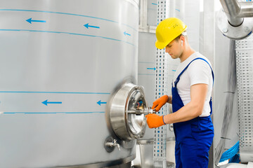 A young chemical plant worker unscrews a threaded valve by opening a hatch in a large tank tank. Work processes in the chemical industry.