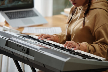 Hands of concentrated girl playing electronic piano at home