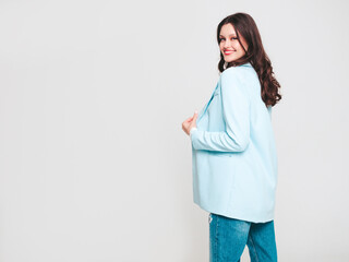 Portrait of young beautiful brunette woman wearing nice trendy blue suit jacket and jeans. Sexy fashion model posing in studio. Fashionable female isolated on white. Cheerful and happy