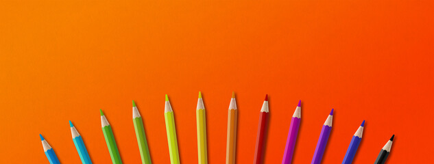Colored pencil group isolated on orange. Panoramic banner background