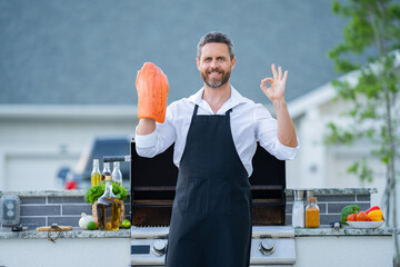 Barbecue master in chef apron hold salmon fillet on BBQ. Middle aged hispanic man in apron for barbecue. Roasting and grilling salmon fillet. Man hold cooking utensils barbecue. Roasting salmon fish.