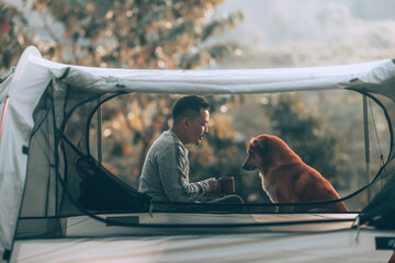 Man drink coffee and relax with dog in the morning during a camping trip in the forest on holiday. Vocation and travel concept.