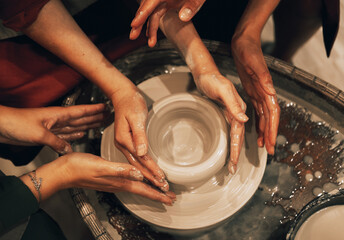 three women are working on a potter's wheel, making a vase.