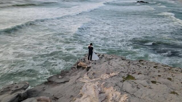 Married couple kiss on a cliff by the ocean