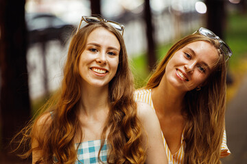 young female friends outdoors in the city. They are sitting while talking at sunset in summer