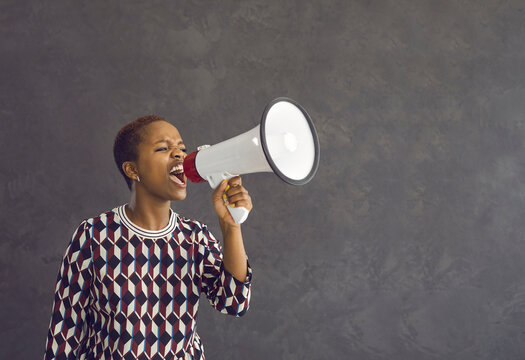 Angry mad young African American woman hold loudspeaker make announcement of deal or sale. Millennial gen z ethnic girl feel motivated get attention screen yell in speaker about good promotion.