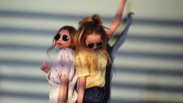 Two Carefree Young Girls Going Crazy. Women in hipster summer clothes having fun and dancing. Positive Smiling Models in Sunglasses. Slow motion. Making Funny Faces