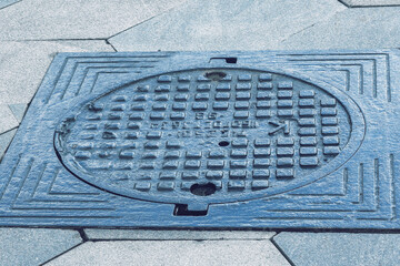 The cover of a sewer manhole on the pavement.