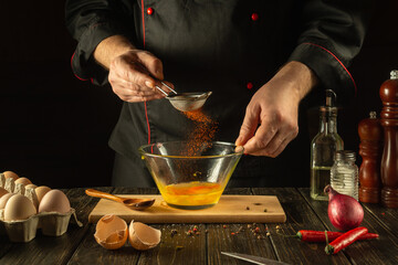 The chef adds paprika to the bowl of eggs. The idea of making a delicious omelet for breakfast. Working environment in a restaurant kitchen