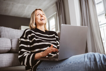 Naklejka premium Young woman sitting on the floor, laughing and looking up at the ceiling with her laptop