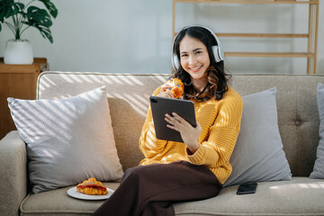 Young Asian woman listening music from headphones and writing note for her work idea in diary book.She in home office or cafe