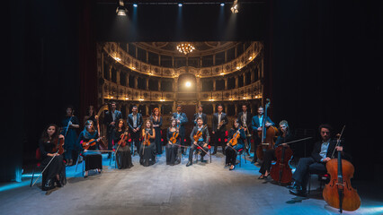 Group Photo: Portrait of Symphony Orchestra Performers on the Stage of a Classic Theatre, Looking at the Camera Together and Smiling. Successful and Professional Musicians Posing 