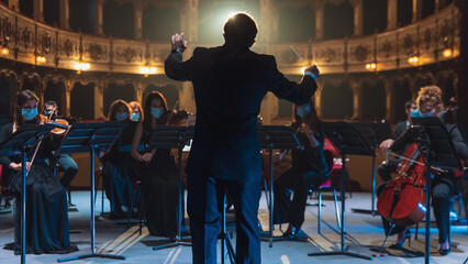 Back View Cinematic shot of Conductor Directing Symphony Orchestra with Performers Playing Violins,...