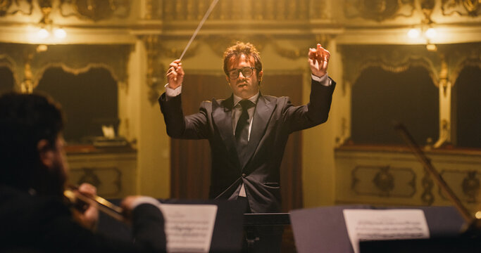 Cinematic Close Up of Conductor Directing Symphony Orchestra with Performers Playing on Stage During Music Concert. Professional Conductor Leading Musicians Passionately in Classic Theater