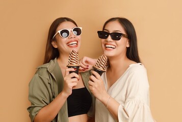 Beautiful young Asian in casual shirt holding big gelato standing over beige background isolated, copy space. Girls Summer joyful concept.