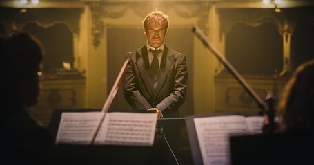 Cinematic Portrait of Male Conductor Standing on Stage Under Spotlight Infront of Symphony...