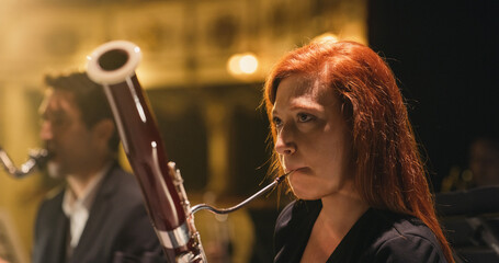 Cinematic Close Up Shot of Professional Female Symphony Orchestra Bassoon Player Performing on Classic Theatre with Curtain Stage during Music Concert. Performers Playing Music for Audience