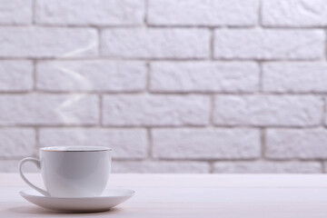 A steaming white cup with a hot drink on a table against a brick wall