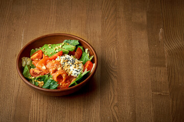 Salad with lightly salted salmon and poached egg in a plate on a wooden background