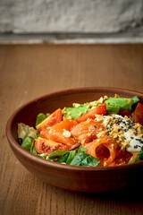 Salad with lightly salted salmon and poached egg in a plate on a wooden background