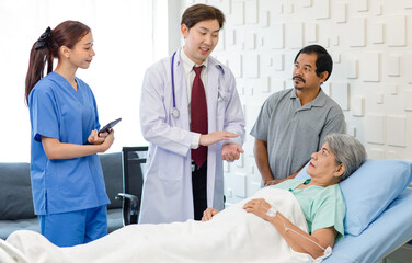Obraz premium Asian professional successful male doctor in white lab coat with stethoscope female assistant internship nurse in blue uniform holding tablet computer visiting old senior unhealthy patient in ward
