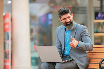 Indian businessman working on laptop and showing thumps up.