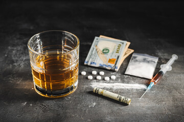 Alcohol drink in a glass, syringe with a dose of drugs, white pills, narcotics powder in a transparent bag and US dollar currency cash on a dark background. Concept of addiction, abuse and bad habits
