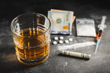 Alcohol drink in a glass, syringe with a dose of drugs, white pills, narcotics powder in a transparent bag and US dollar currency cash on a dark background. Concept of addiction, abuse and bad habits