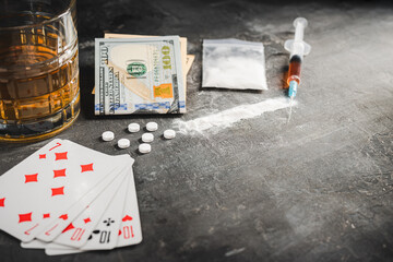 Alcohol drink in a glass, playing cards for poker game, syringe with a dose of drugs, white pills, powder narcotics and US dollar currency on dark background. Concept of addiction, gambling and abuse