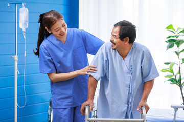 Fototapeta premium Asian professional successful female internship nurse in blue uniform smiling visiting helping supporting old senior elderly pensioner male patient physical therapy walking with four legged walker