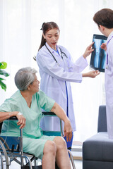 Obraz premium Asian young professional successful male and female doctor in white lab coat with stethoscope standing holding leg bone xray film showing to old senior pensioner injury patient sitting on wheelchair