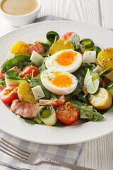 Peasant salad prepared with leafy vegetables, ham, cheese, tomatoes, potatoes and soft-boiled eggs closeup on the table. Vertical
