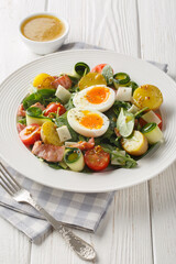 Fresh peasant salad with arugula, spinach, potatoes, bacon, tomatoes, cheese and soft-boiled eggs close-up on a plate on the table. Vertical