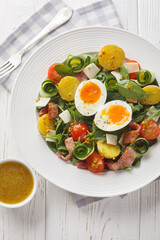 Peasant salad prepared with leafy vegetables, ham, cheese, tomatoes, potatoes and soft-boiled eggs closeup on the table. Vertical top view from above