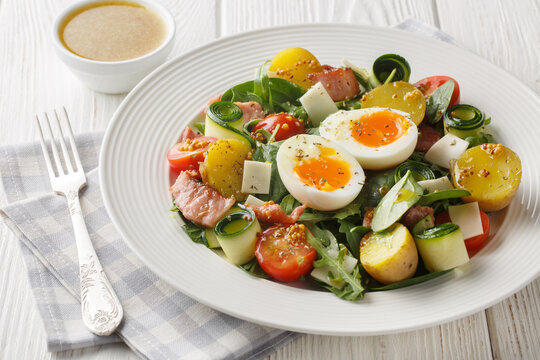 French peasant salad or salade paysanne with lettuce, bacon, cheese, tomatoes, potatoes and soft-boiled eggs closeup on the table. Horizontal