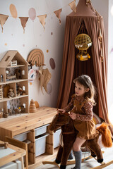 A little girl in a Scandinavian children's room on a horse. Game nursery with a canopy. Containers for storage of toys. Dollhouse.