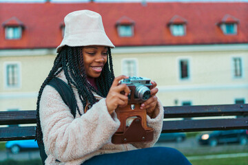 Portrait of a beautiful black woman smiling excitedly at the camera, she's wearing a bucket hat and a backpack, she's drinking coffee and taking pictures with her phone