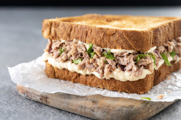 Tuna sandwich with mayo and vegetables on gray stone background.