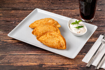 Beef Cheburek on a wooden table. Deep Fried Beef Dumplings with meat and onions. Turkish name Ci Borek or Cig Borek
