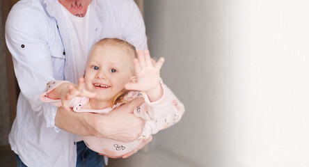 Young dad is playing with a charming little daughter. The man holds the girl on hands and is turned...