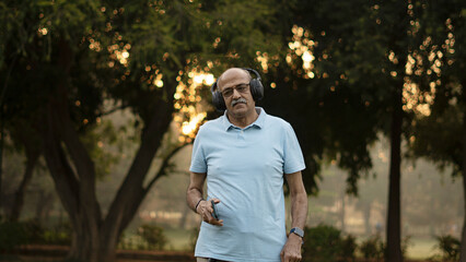 Obraz premium Happy senior citizen man in park listening music in headphones