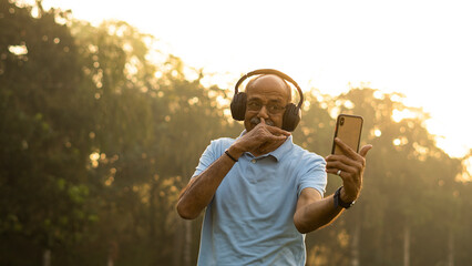 Fototapeta premium Happy senior citizen man in park listening music in headphones