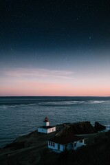 Aerial shot of a lighthouse and another building on the coast of a wavy sea under the sky at sunset