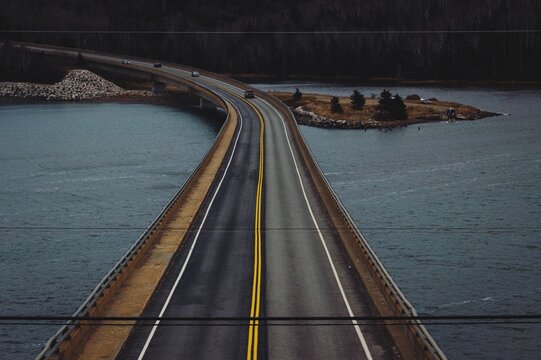 Aerial shot of cars driving on a road built on a bridge over a lake in a park in Nova Scotia